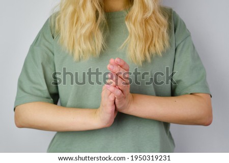 Blond hair woman posing near a light wall. Beautiful young caucasian girl. Hand gestures. Emotion. Casual clothing. Studio model in work. Strong woman, future is female. Jeans and green blank t-shirt