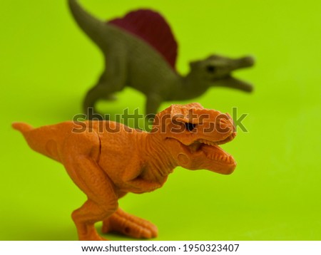 Isolated orange T-Rex and green Spinosaurus dinosaur figures made from erasers against lime green background