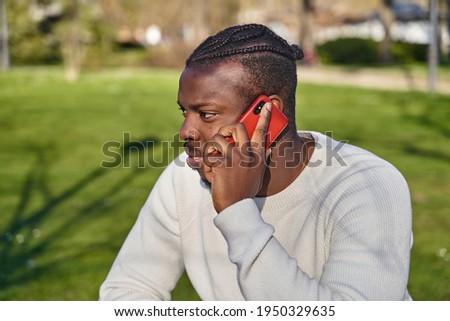 Portrait of young African American man talking on cell phone in a park. Black man with braids in his hair. High quality photo