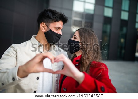 Portrait of a couple wearing masks and doing the heart sign with their hands, covid and coronavirus love concept
