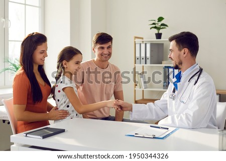 Little girl and her family in consultation with a pediatrician. Child shakes hands and meets the family doctor while sitting in the doctor's office. Concept of pediatrics and health insurance. Royalty-Free Stock Photo #1950344326