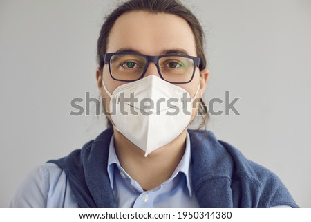 Close up headshot of happy young guy wearing eyeglasses and breathing through FPP2 KN95 N95 face mask to protect from polluted air or Covid 19 viral infection in times of global coronavirus pandemic Royalty-Free Stock Photo #1950344380