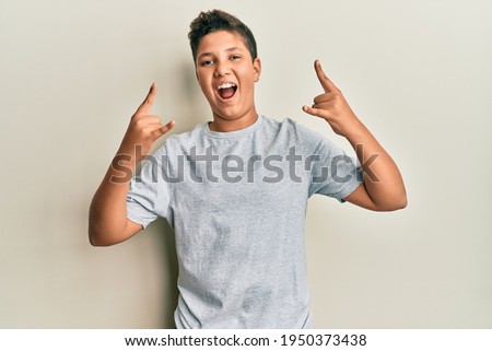 Teenager hispanic boy wearing casual grey t shirt shouting with crazy expression doing rock symbol with hands up. music star. heavy concept. 