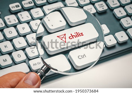 Cryptocurrency trading concept: Male hand holding magnifying glass and focusing computer key with chiliz | chz logo. Cryptocurrency mining, trading, market concept.