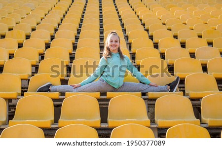 Happy girl gymnast do splits stretching legs on stadium seats, gymnastics