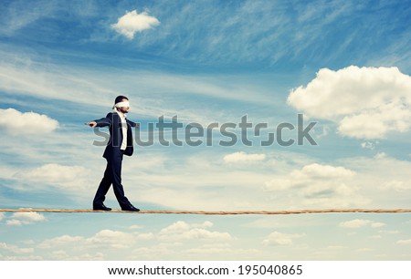 man with the blindfold walking on the rope over blue sky Royalty-Free Stock Photo #195040865