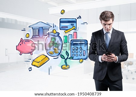 Young serious businessman stays in office and holds smart phone and while looking up for new ways and methods of earning money. Financial sketch in the foreground. Concept of financial management