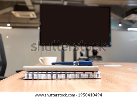 Close up pen and notebook on table with blank display television in meeting room