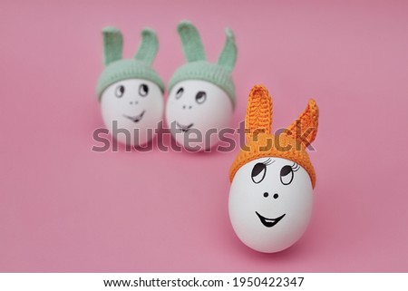 funny egg in orange cap with ears on pink background and two eggs in green caps