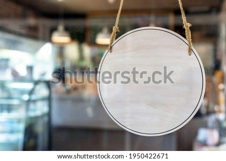 blank vintage wooden sign board hanging on glass door in modern cafe restaurant, copy space for text advertising, advertisement marketing and small business owner concept