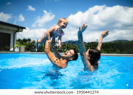 Young family with small daughter in swimming pool outdoors in backyard garden, playing. Royalty-Free Stock Photo #1950441274