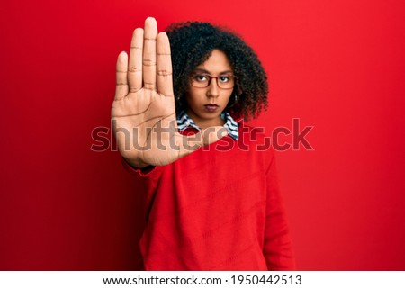 Beautiful african american woman with afro hair wearing sweater and glasses doing stop sing with palm of the hand. warning expression with negative and serious gesture on the face. 