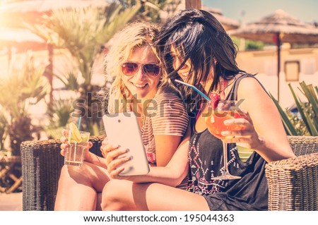 Two girls looking at phone outdoor drinking cocktails