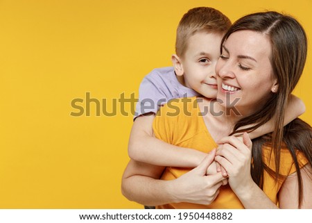 Happy young woman have fun with cute child baby boy 5-6-7 years old in violet t-shirt. Mommy little kid son posing together hugs isolated on yellow background studio. Mother's Day love family concept