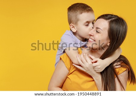 Happy young woman have fun with cute child baby boy 5-6-7 years old in violet t-shirt. Mommy little kid son posing together hugs isolated on yellow background studio. Mother's Day love family concept Royalty-Free Stock Photo #1950448891