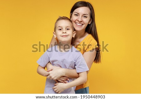 Happy young woman have fun with cute child baby boy 5-6-7 years old in violet t-shirt. Mommy little kid son posing together hugs isolated on yellow background studio. Mother's Day love family concept Royalty-Free Stock Photo #1950448903