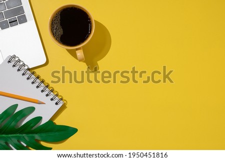 Desk top view on yellow background. Flat lay, top view office table desk. Workspace with Laptop, keyboard, coffee, pencil, green leaf and blank note.