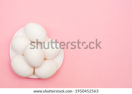 White chicken eggs on a white plate on a pink background 