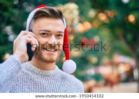 Young caucasian man wearing christmas hat talking on the smartphone at the park