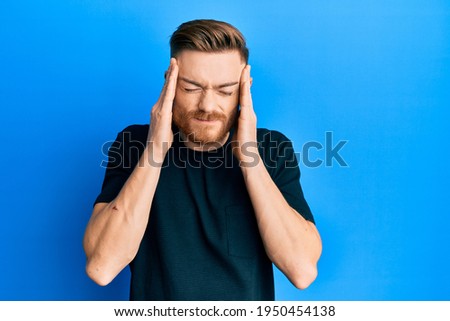 Young redhead man wearing casual black t shirt with hand on head, headache because stress. suffering migraine. 