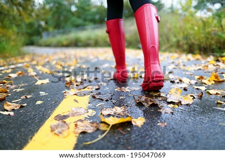 Autumn fall concept with colorful leaves and rain boots outside. Close up of woman feet walking in red boots. Royalty-Free Stock Photo #195047069