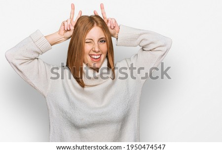 Young irish woman wearing casual winter sweater posing funny and crazy with fingers on head as bunny ears, smiling cheerful 