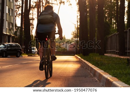 Cyclist with backpack rides on road bicycle on asphalt road in the city at sunset. Bicycle commuting.