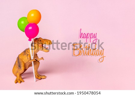 Toy dinosaur Tyrannosaurus holding colorful balloons in its paws on pink background Holiday card Happy birthday creative minimal concept 