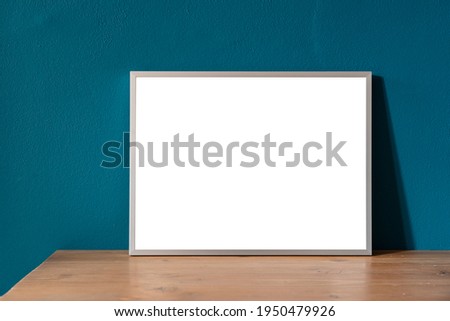 Mockup of a picture frame with a white interior on a wooden shelf with the wall of the living room of a house painted in petrol green