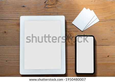 Selected objects arranged on a wooden work table: smartphone tablets with empty display and white business cards to fill with the company or brand graphics - Mockup business