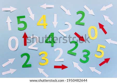 Random arrangement of many colorful numbers and arrows on blue paper.
