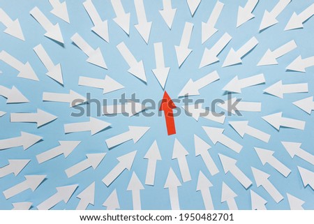 One red arrow pointing up surrounded with many white paper arrows on blue paper background.