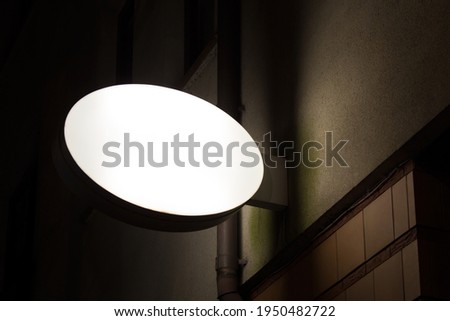Round glowing light box mockup template at night hanging on the building exterior wall.