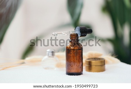 Opened brown glass dropper bottle with pipette with black rubber tip on the background of green natural leaves in the bathroom. Skin concept. Organic spa cosmetics. Fashionable concept.