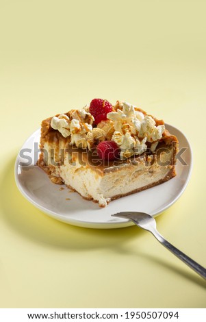 Toffee Popcorn Cheesecake  with raspberry and popcorn in the top on yellow background 