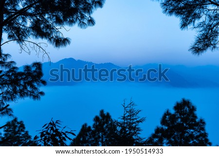 A view of mountains and valley covered in early morning fog and mist with trees framing the corners of the image