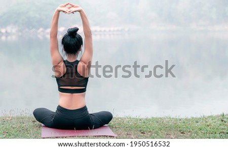 Reae view of young woman in sportswear exercising before doing yoga near the lake.