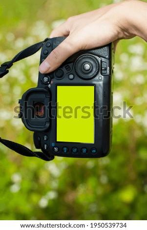 hand holds the camera. female hands with a camera, holds to photograph, green background. close-up, concept of tourism, travel, hobby, blogger. black camera, screen.