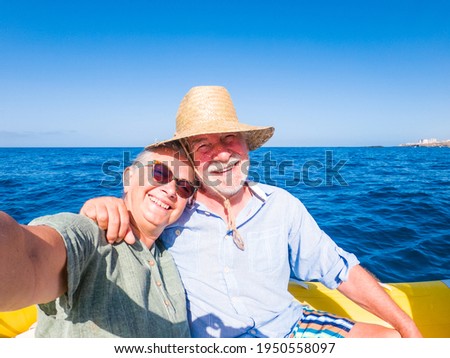 Beautiful and cute couple of seniors or old people in the middle of the sea driving and discovering new places with small boat. Mature woman holding a phone and taking a selfie with hew husband