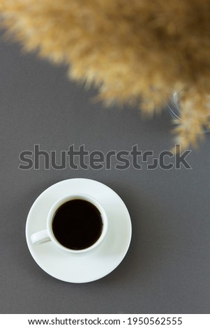 One cup of aromatic black coffee on a trendy gray background. Nearby there is pampas grass as a decorative element. Top view, place for text.