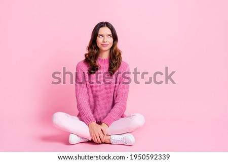 Full size photo of optimistic cool brunette lady sit look empty space wear pink sweater trousers sneakers isolated on pink background