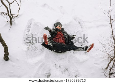 A fearless, strong man, a stuntman, a stuntman in a black coat falls from a great height on the white snow in winter. Photography, concept. Shooting a motion picture.