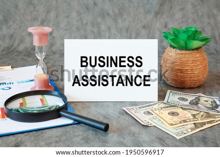 Business Assistance is written in a document on the office desk with office accessories, money and diagram