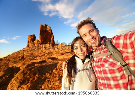 Selfie - Happy couple taking self portrait photo hiking. Two lovers or friends on hike smiling at camera outdoors mountains by Roque Nublo, Gran Canaria, Canary Islands, Spain.