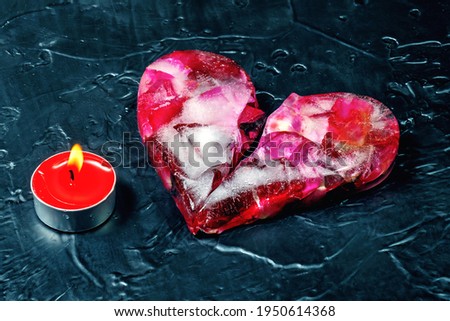 Pink icy heart split in half and burning candle on a black background. Close-up. 

