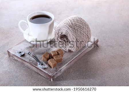 A cup of coffee on a tray and a skein of natural wool next to it. Hobby concept. Free space. Top view. Light background.