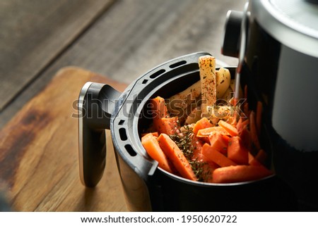 Cooking potatoes and carrot sticks with spices in an air fryer Royalty-Free Stock Photo #1950620722