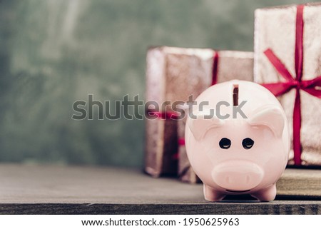 Piggy bank on wooden table on background of gift boxes. Copy space for text. Concept of investing and storing finance