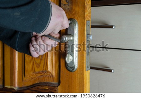 A man removes the old door lock. Hands with a screwdriver unscrew the mounting screws of the mortise lock of a wooden interior door. Services to repair or replace furniture fittings. Indoors Royalty-Free Stock Photo #1950626476