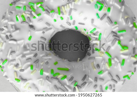 Flat-lay image of ring donut with white glaze and hundreds and thousands, black and white image with selected green colour
